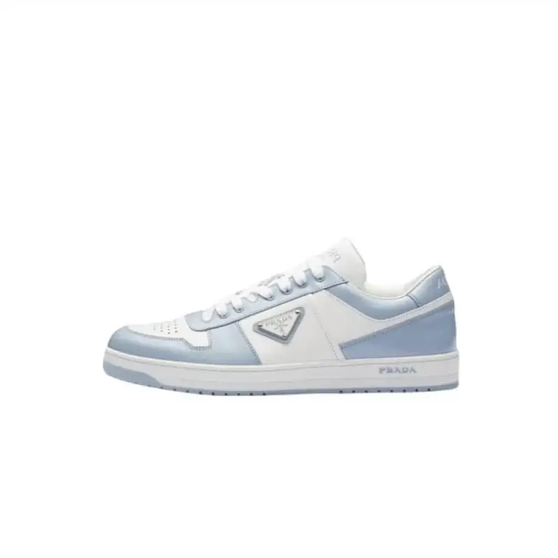 A sleek and stylish Prada low-top sneaker featuring a white and light blue color-block design, with a metallic triangular logo on the side and “PRADA” branding on the heel and midsole, exuding a clean, elegant look with premium craftsmanship.